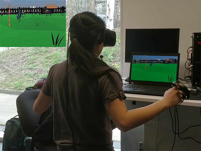 A girl with a VR headset on, facing a laptop and raising their arms whilst holding VR controllers.